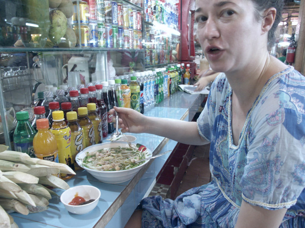 Eine Frau im blauen Kleid isst eine scharfe Nudelsuppe im Ben Thanh Markt Saigon