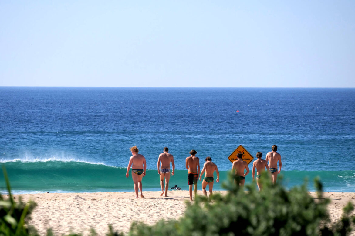 Gruppe von Männern am Tamarama Strand in Sydney gehen zum türkisblauen Ozean