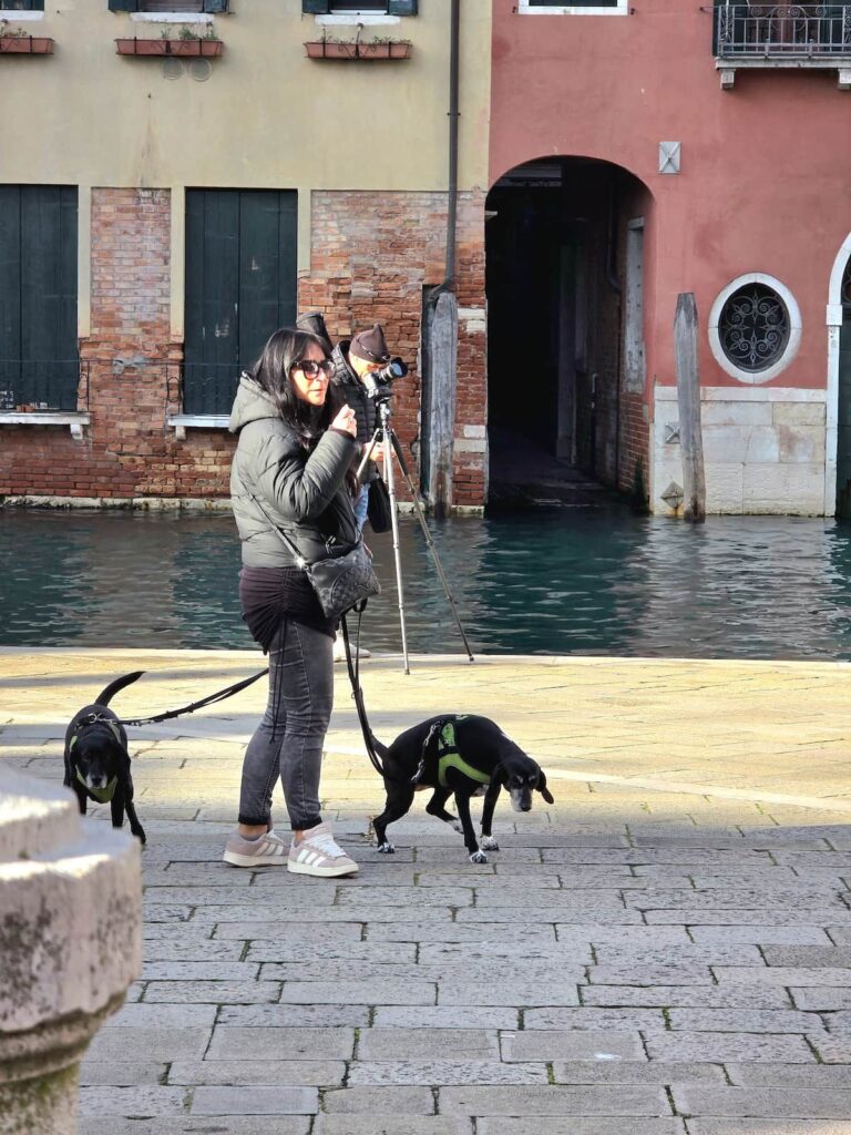 Zwei schwarze Hunde und eine Frau auf einem Platz beim Kanal in Venedig